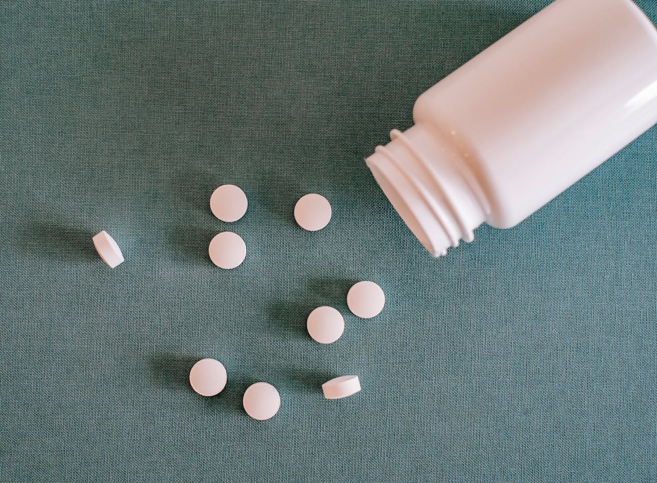 White pills spilling from a plastic bottle on a teal surface, captured in a top view layout.